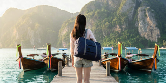 Voyageur avec un sac de voyage pliable sur un ponton de la mer d'Andaman en janvier, longtails et falaises karstiques